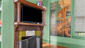 A fireplace with a television above it, a mural on the wall, and a window with blinds. - The Gilded Jaguar - w/King Bed in Riverside (Jacksonville)