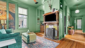 A room with a fireplace, green walls, a sofa, and a patterned rug. - The Gilded Jaguar - w/King Bed in Riverside (Jacksonville)