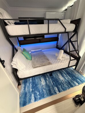 A bunk bed with a blue textured mat at the bottom, white bedding, and a small green pillow. - Unique 2-bedroom modular home in Jobos Isabela's countryside, near beaches! (Jobos)