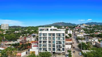 Un hôtel à plusieurs étages doté de balcons, d’une cour intérieure et offrant une vue sur le paysage urbain et les collines environnantes.