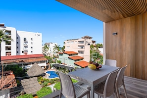 A balcony with a table and chairs, overlooking a pool and buildings. - 3BR Condo Near the Ocean in Bucerías With Pool, Wifi & Full Kitchen (Bucerías)