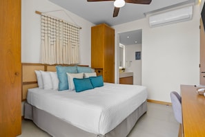 A bedroom with a bed, a ceiling fan, a wall-mounted air conditioner, and a wooden door. - 2BR Near the Ocean With Pool, Gym, Wifi, and Full Kitchen (La Cruz de Huanacaxtle)