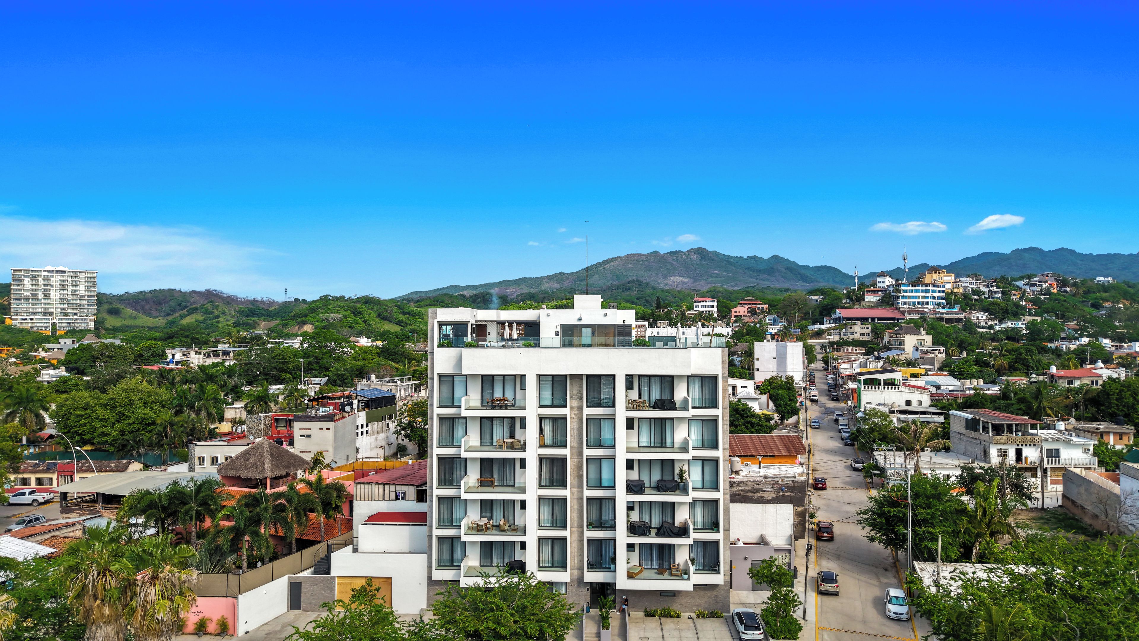 Un hotel de varios pisos con balcones, un patio central y vistas del entorno urbano y las colinas.