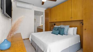 A bedroom with a bed, wooden wardrobe, ceiling fan, and a TV on the wall.