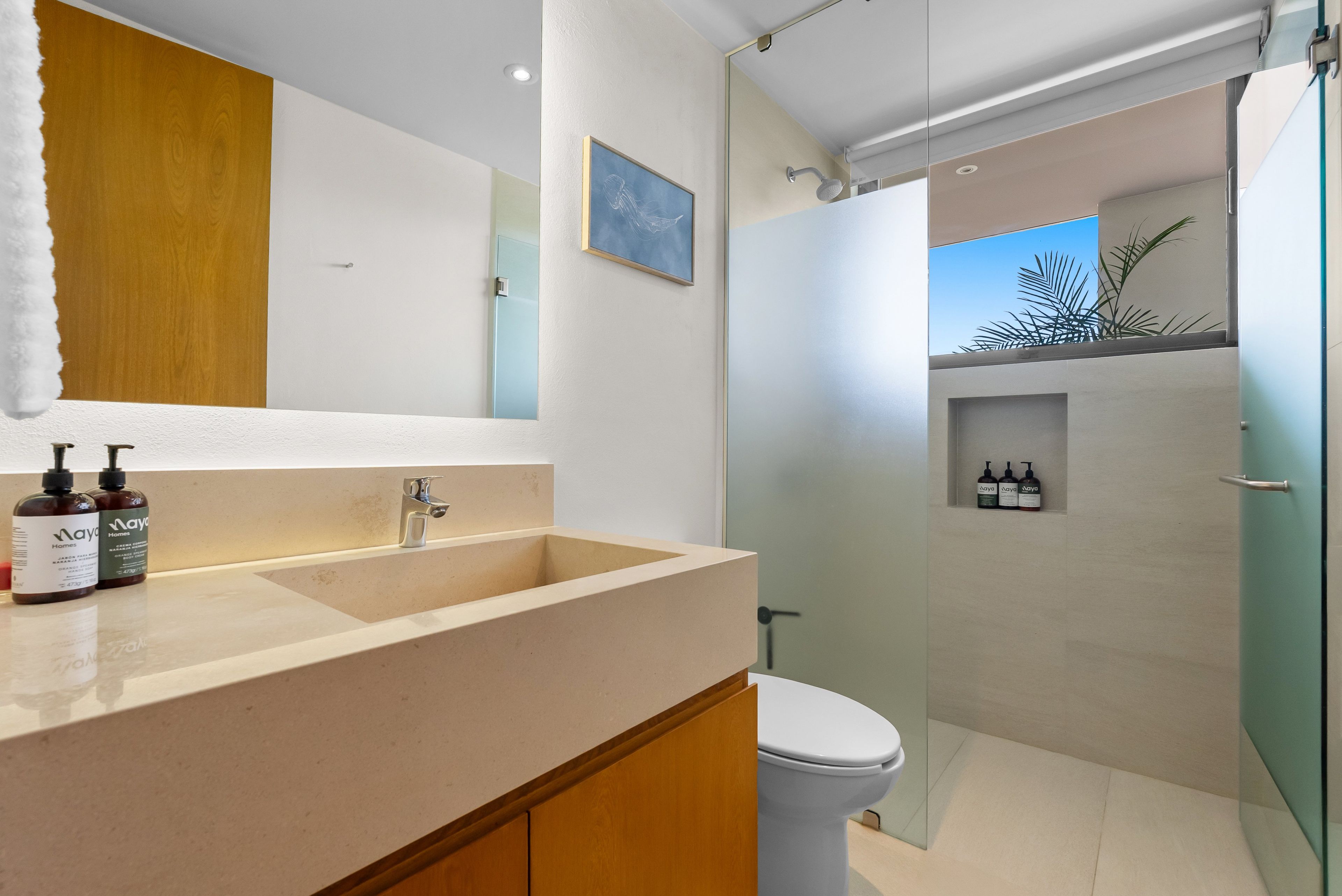 Ein Badezimmer mit großem Spiegel, Waschbecken mit zwei Shampooflaschen, Toilette und Duschbereich.