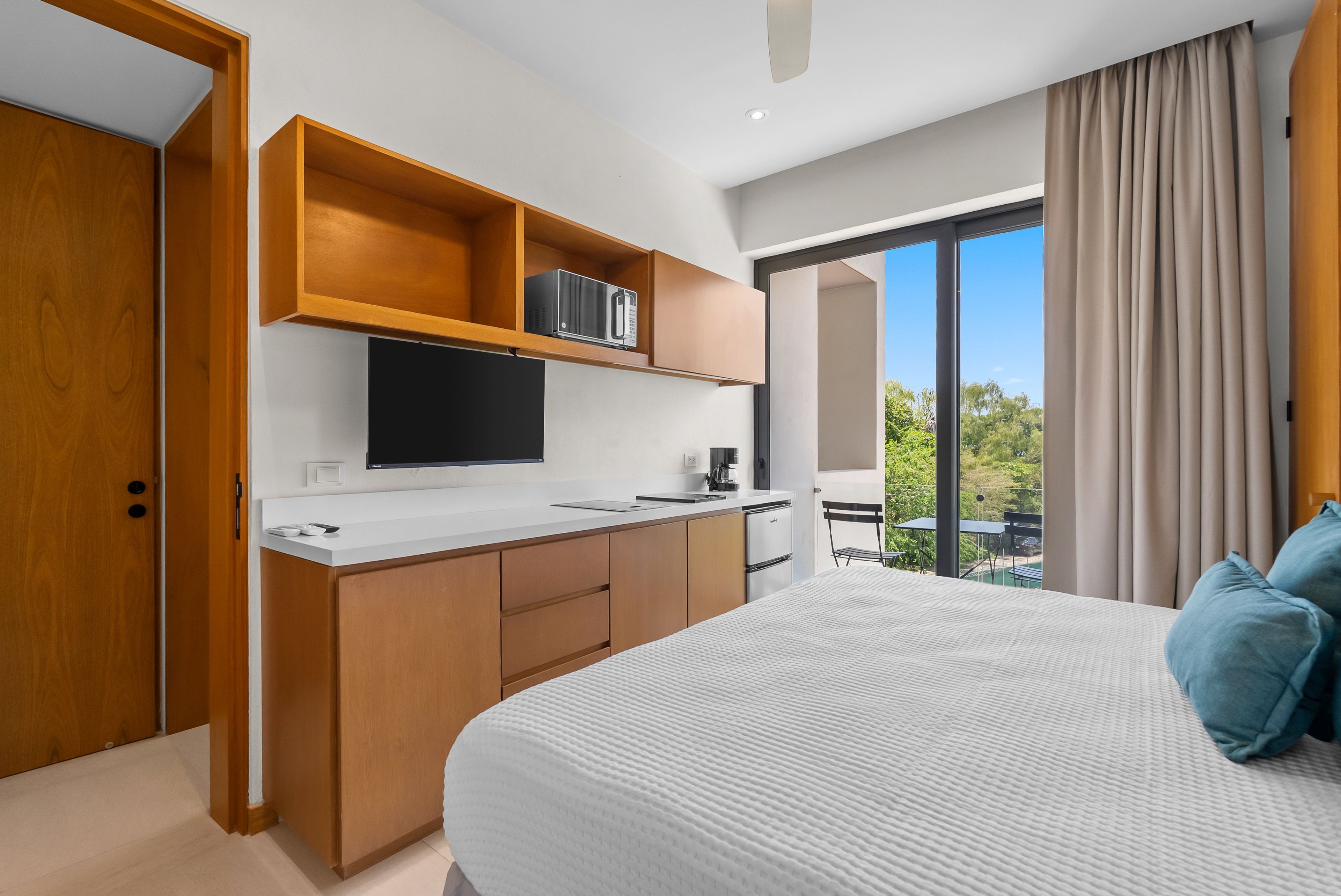A modern bedroom with a large bed, a built-in TV, and a kitchenette.