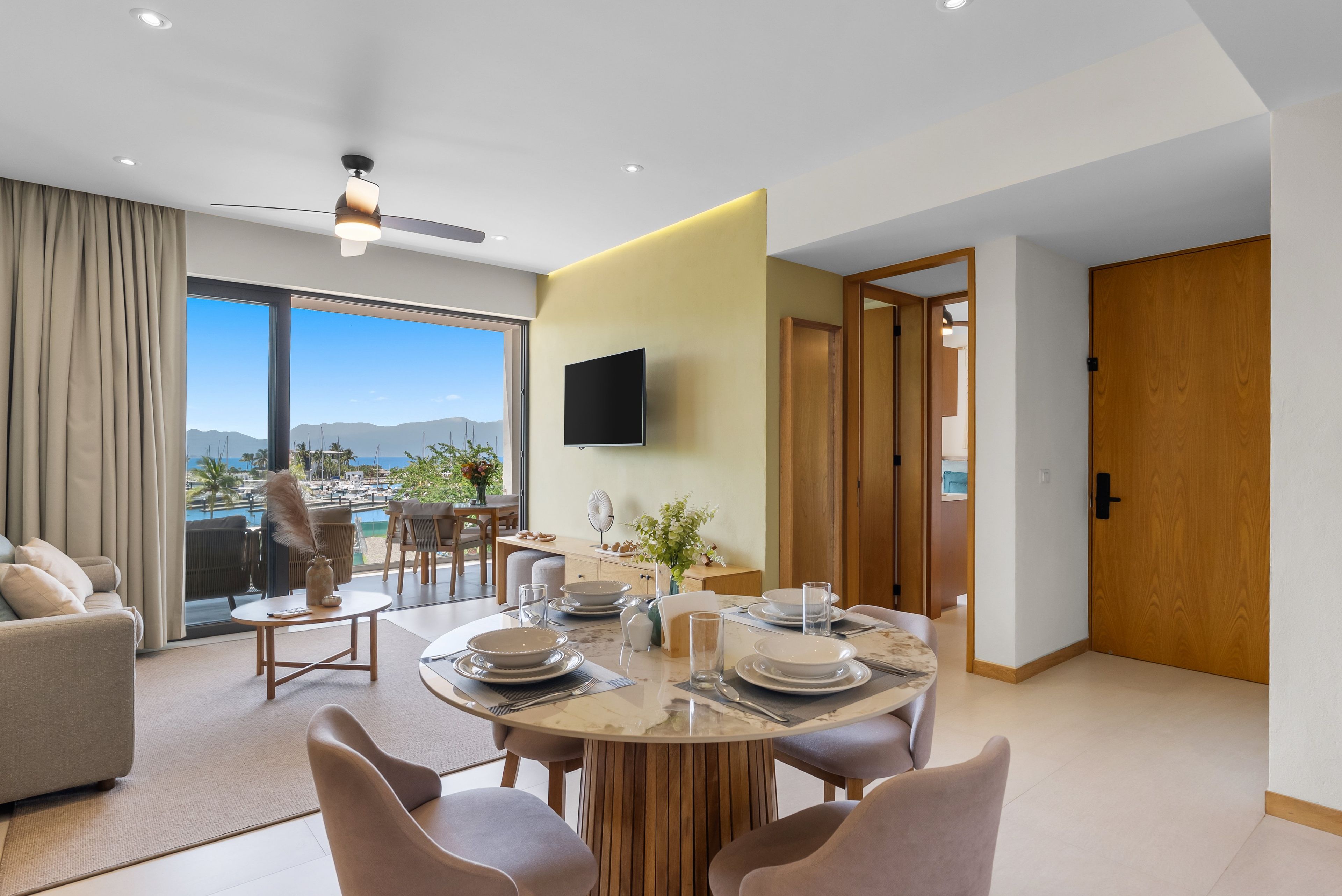 A modern dining area with a round table, chairs, and a view of a marina.