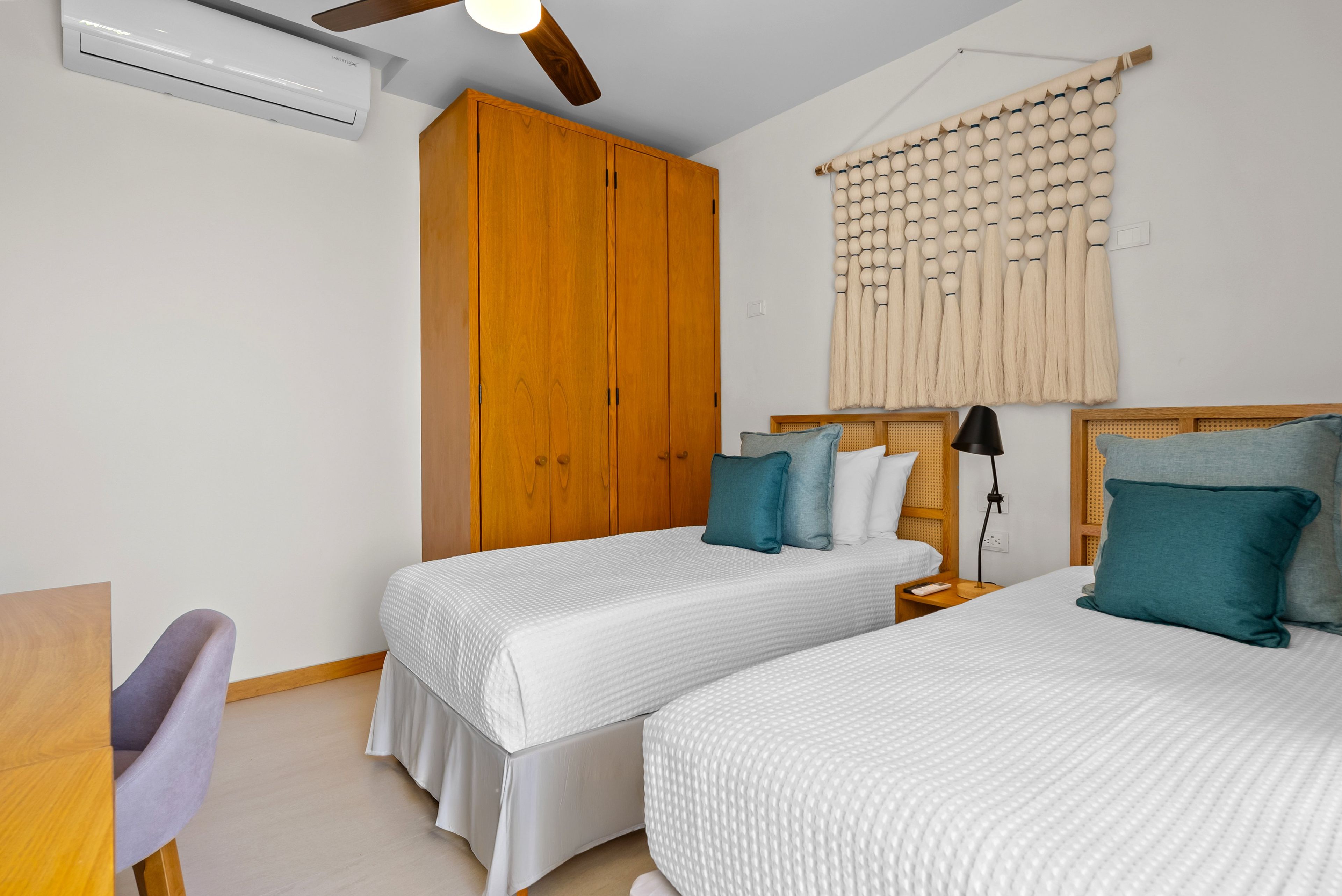 Une chambre avec deux lits, une armoire en bois, un ventilateur de plafond et un rideau fixé au mur.