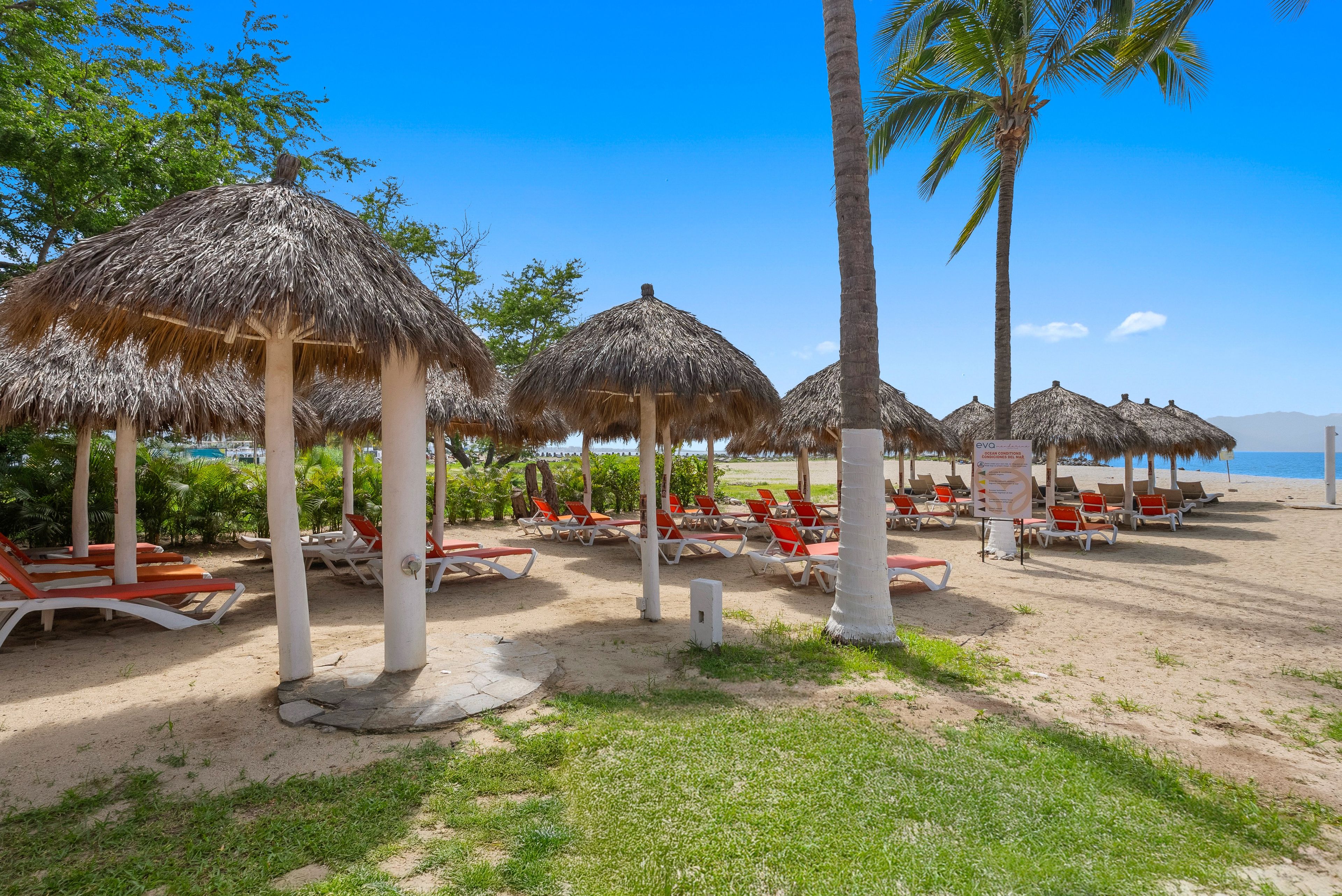 Un resort frente al mar con sombrillas de paja, sillas de playa y palmeras.