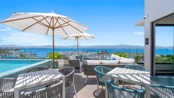 Une terrasse avec des sièges extérieurs, une piscine et une vue sur le port de plaisance et la mer.