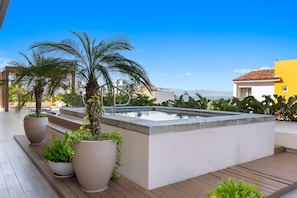 A rooftop pool area with a clear view of the ocean, surrounded by potted plants and a wooden deck. - Cozy 1BR Bucerías Stay With Pool, Gym, Wifi & Kitchenette (Bucerías)