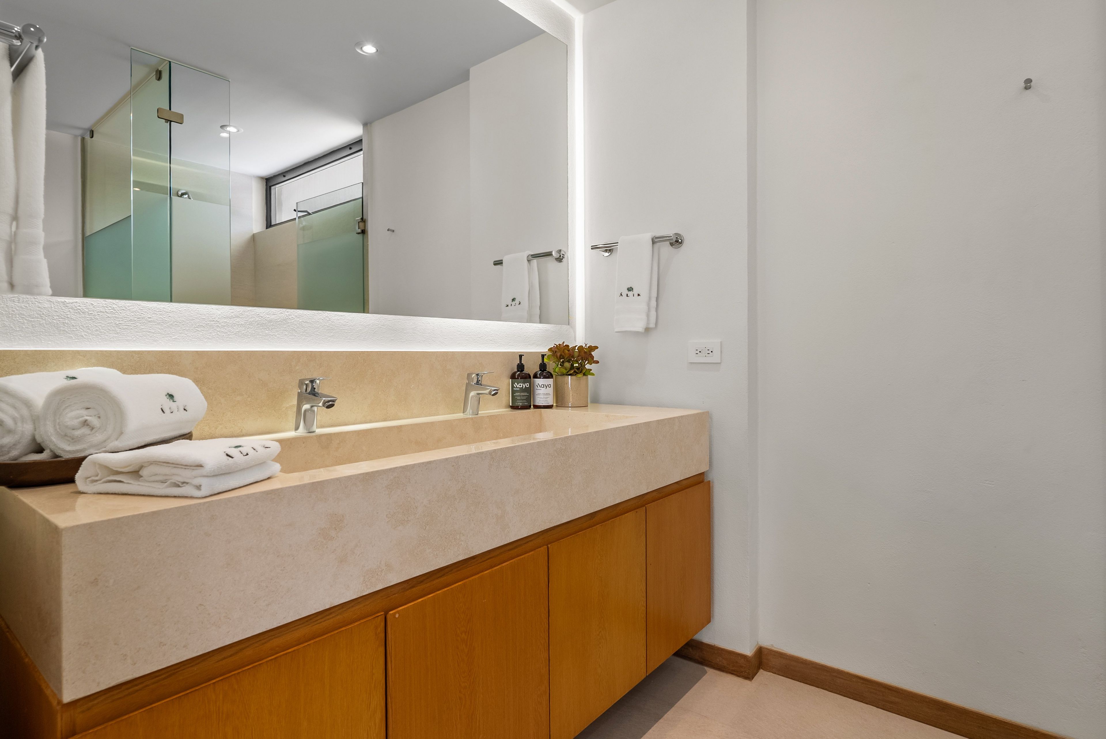 A modern bathroom with a large mirror, a sink with a beige countertop, wooden cabinets, and a towel rack with towels.