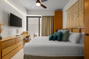A modern bedroom with a bed, a flat-screen TV, a wooden dresser, a chair, and a ceiling fan. - New Home 1BR Condo in La Cruz With AC, Pool, Wifi, Balcony, and Full Kitchen (La Cruz de Huanacaxtle)