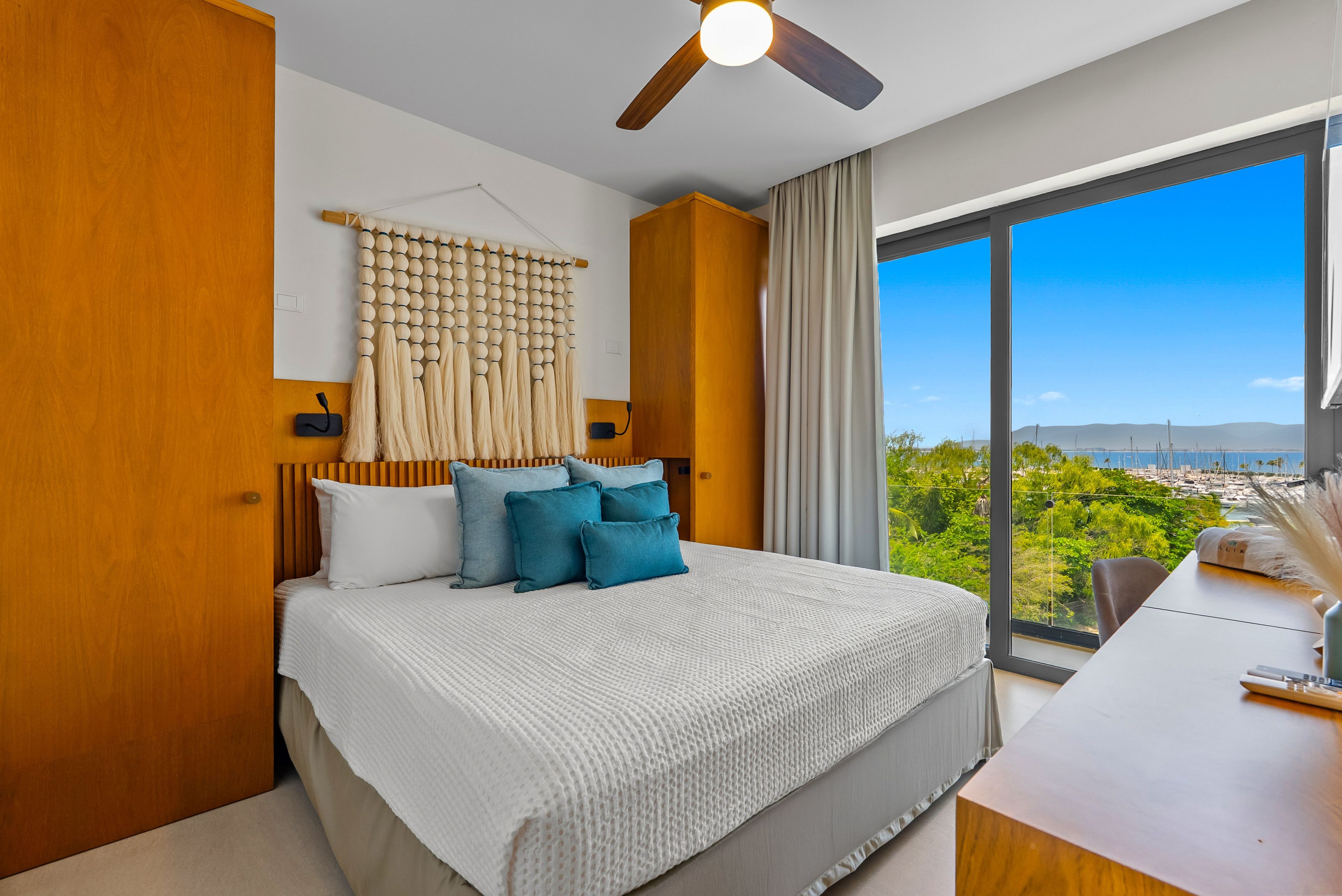 A modern bedroom with a large bed, a ceiling fan, and a view of a marina through a large window.