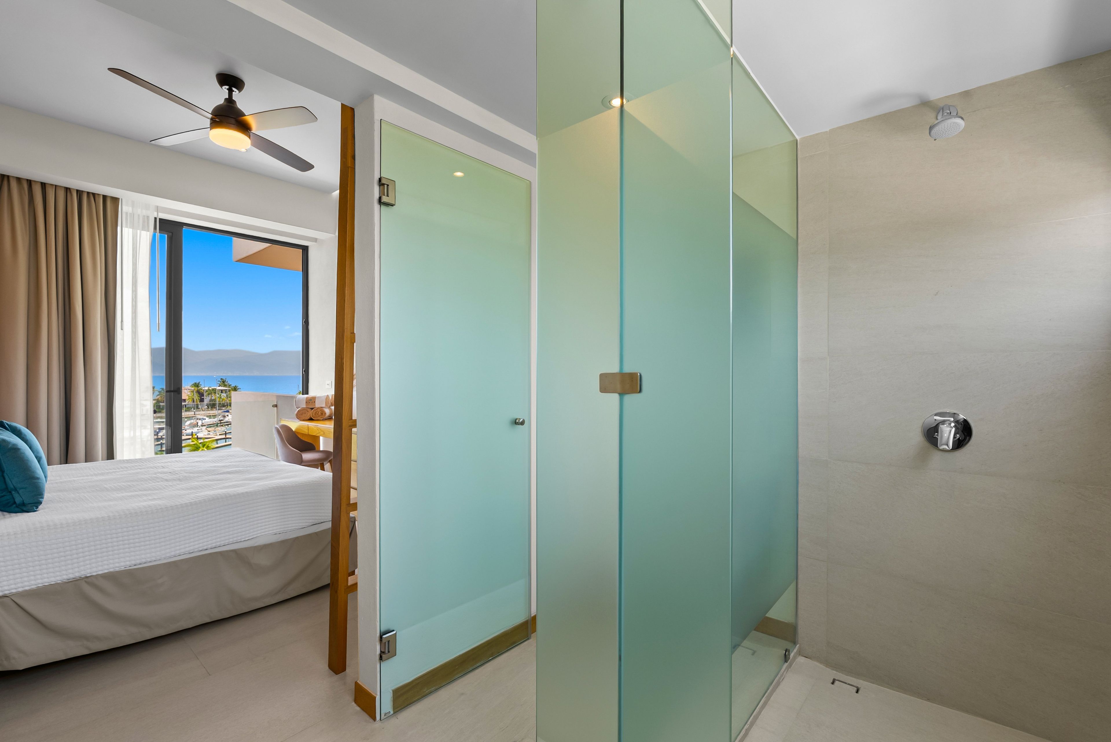 Habitación de hotel con cama, escritorio, silla, ventilador de techo y vista al mar.