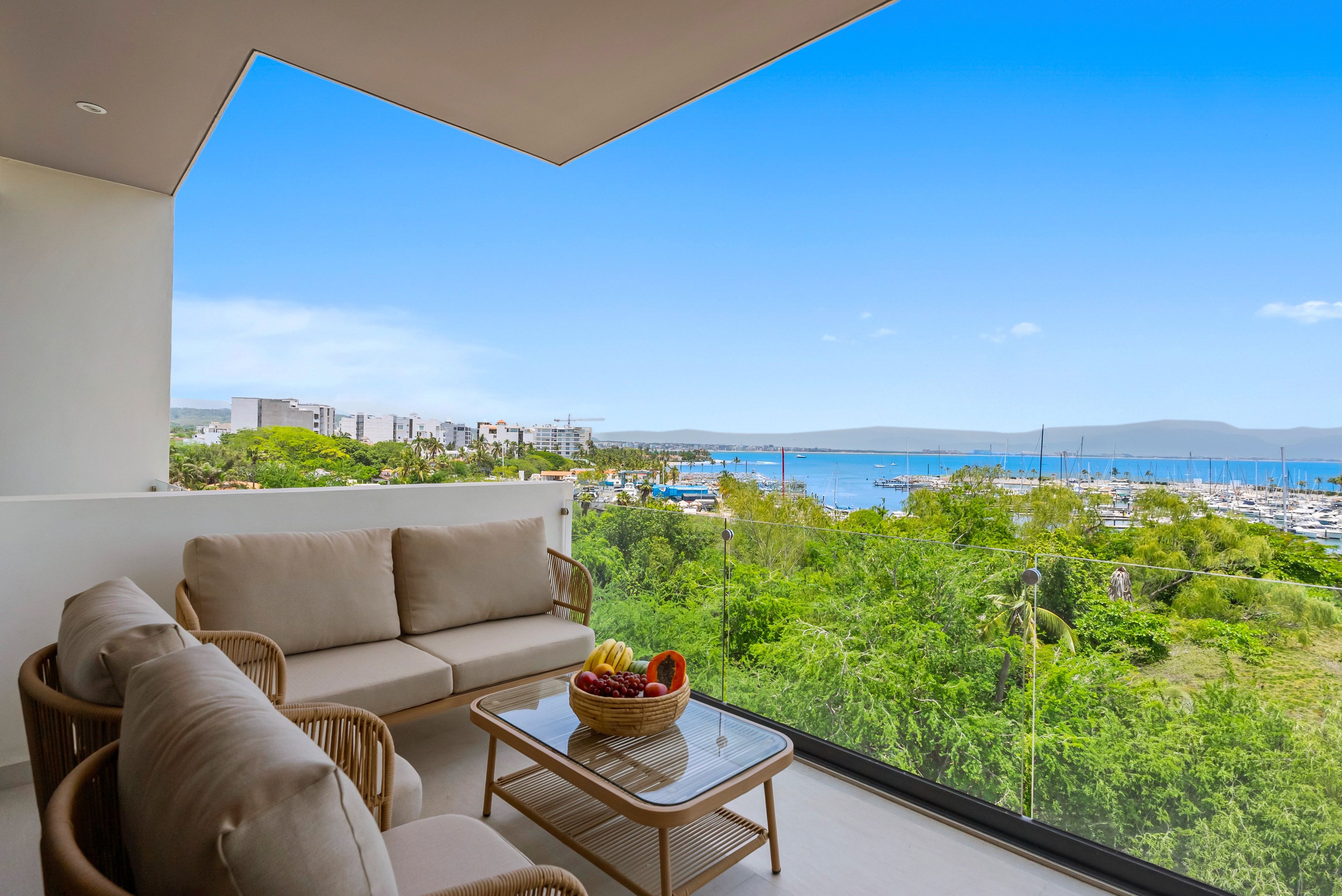 Balcón con sofá y mesa, con vistas a un puerto deportivo y zonas verdes.