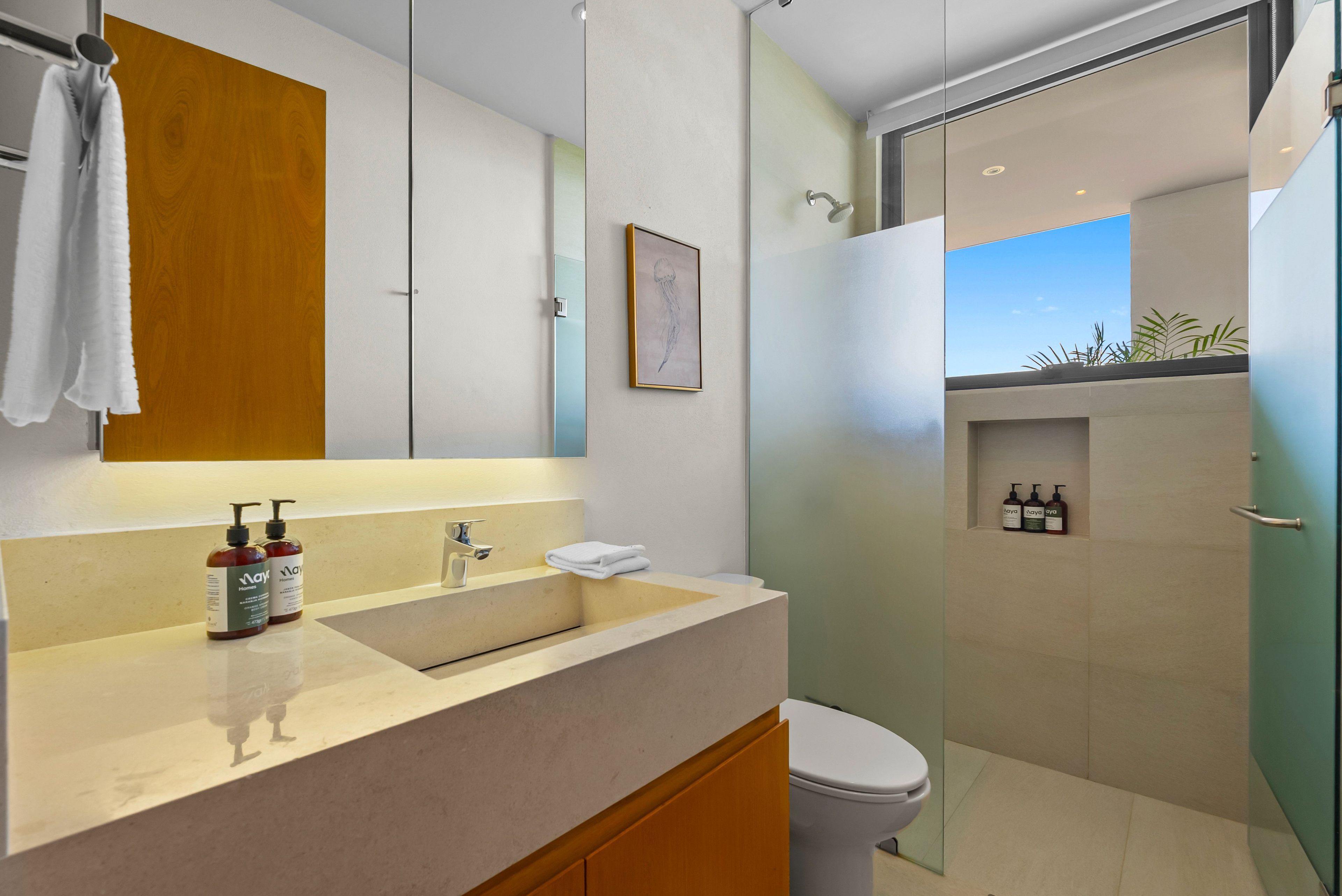 Un baño moderno con un espejo grande, un lavabo con dos botellas de champú, un inodoro y una zona de ducha.
