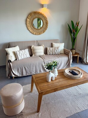 A living room with a sofa, a coffee table, a round mirror, and a potted plant. - Spacious apartment with a garden just a stone's throw from the beach (Saint Martin)