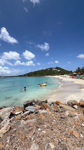 A beach with clear turquoise water, rocky foreground, and a hilly backdrop with buildings. - Spacious apartment with a garden just a stone's throw from the beach (Saint Martin)