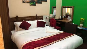 Una habitación de hotel con cama, escritorio, silla, espejo y pared verde.