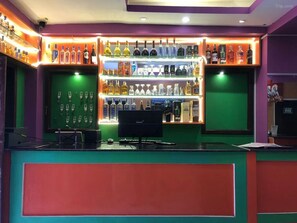 Zona de bar con estanterías llenas de botellas y una barra con un ordenador.