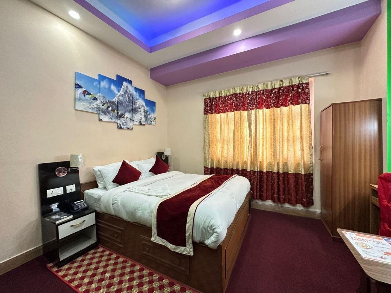 Habitación de hotel con cama, mesita de noche, lámpara, una obra de arte en la pared y una ventana con cortinas.