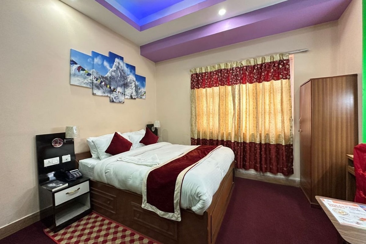 Habitación de hotel con cama, mesita de noche, lámpara, una obra de arte en la pared y una ventana con cortinas.