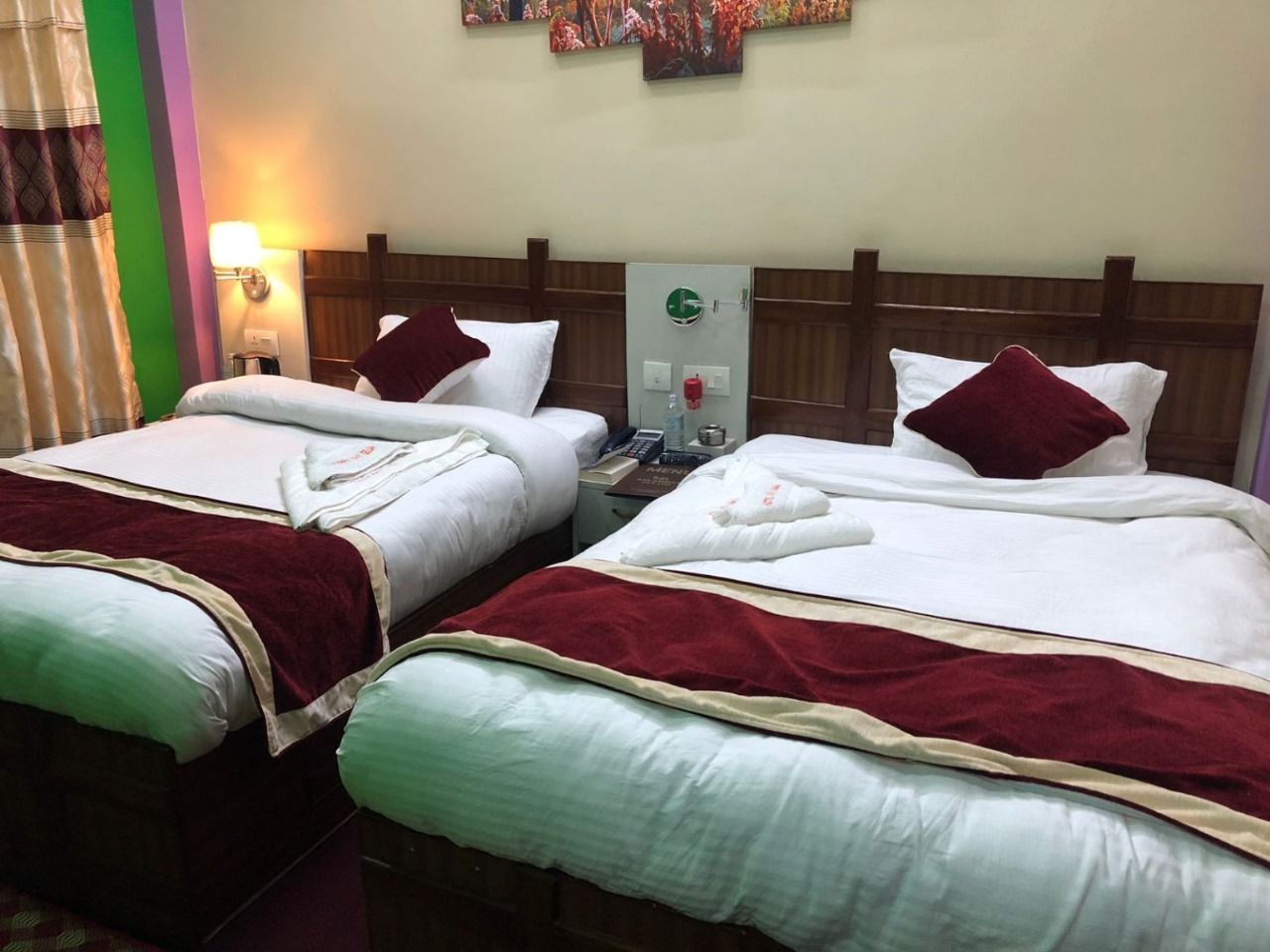 Habitación de hotel con dos camas, cada una con cubrecolcha rojo y blanco, cabecero de madera y mesita de noche con lámpara y teléfono.