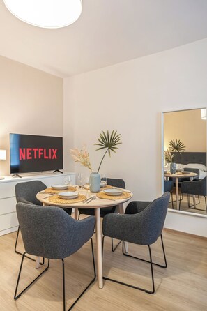 A modern dining area with a round table, four grey chairs, and a television displaying the Netflix logo. - Apartment with a view of the garden & air conditioning | Danube Canal | 6 guests (Wien)