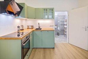 A modern kitchen with a wooden countertop, stainless steel appliances, and light green cabinetry. - Apartment with a view of the garden & air conditioning | Danube Canal | 6 guests (Wien)