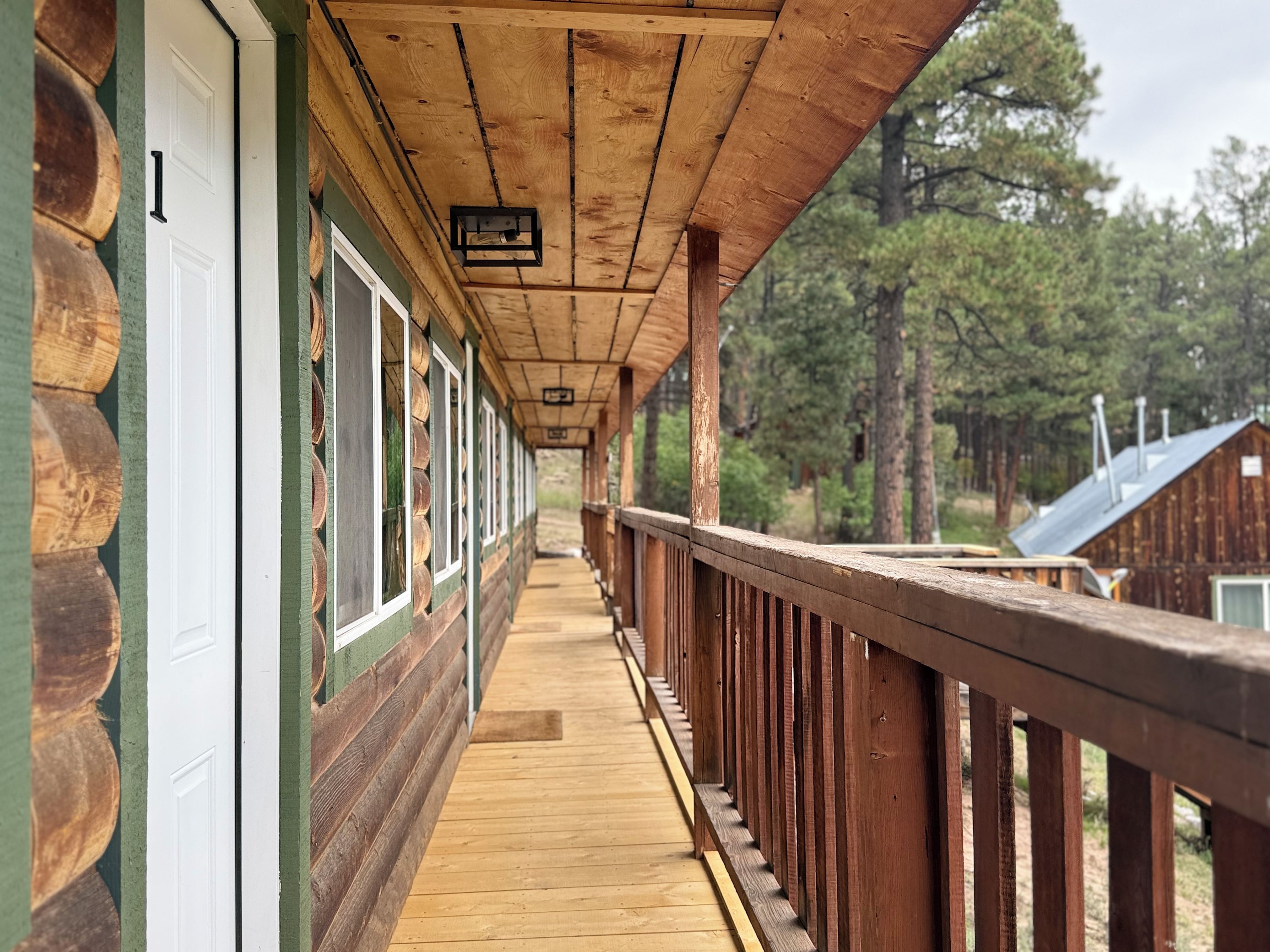 A wooden corridor with a wooden railing, a wooden floor, and a door on the left.