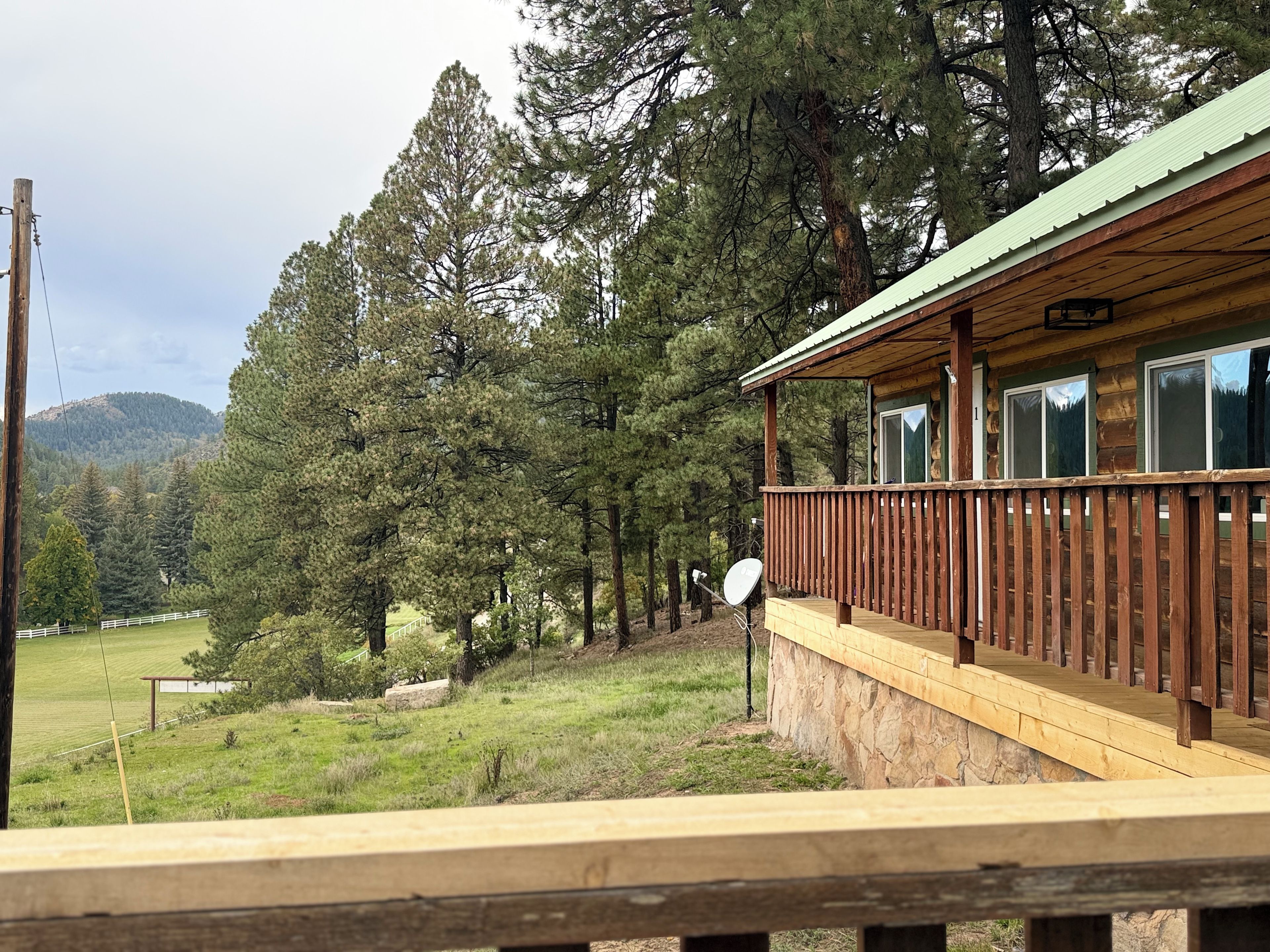 A wooden cabin with a balcony, surrounded by trees and a grassy field.