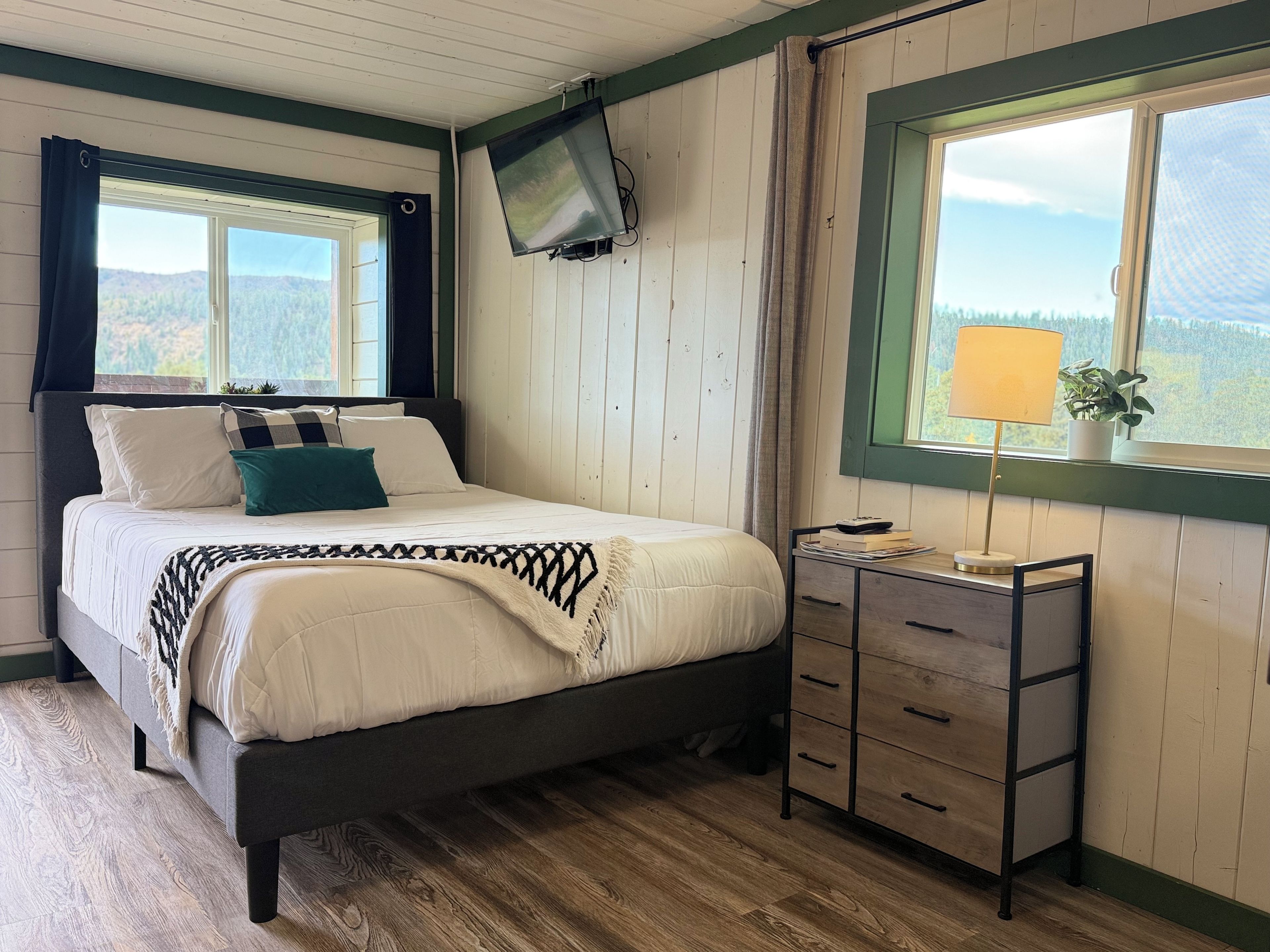 A bedroom with a bed, a nightstand, a lamp, and a window with a view of the outdoors.