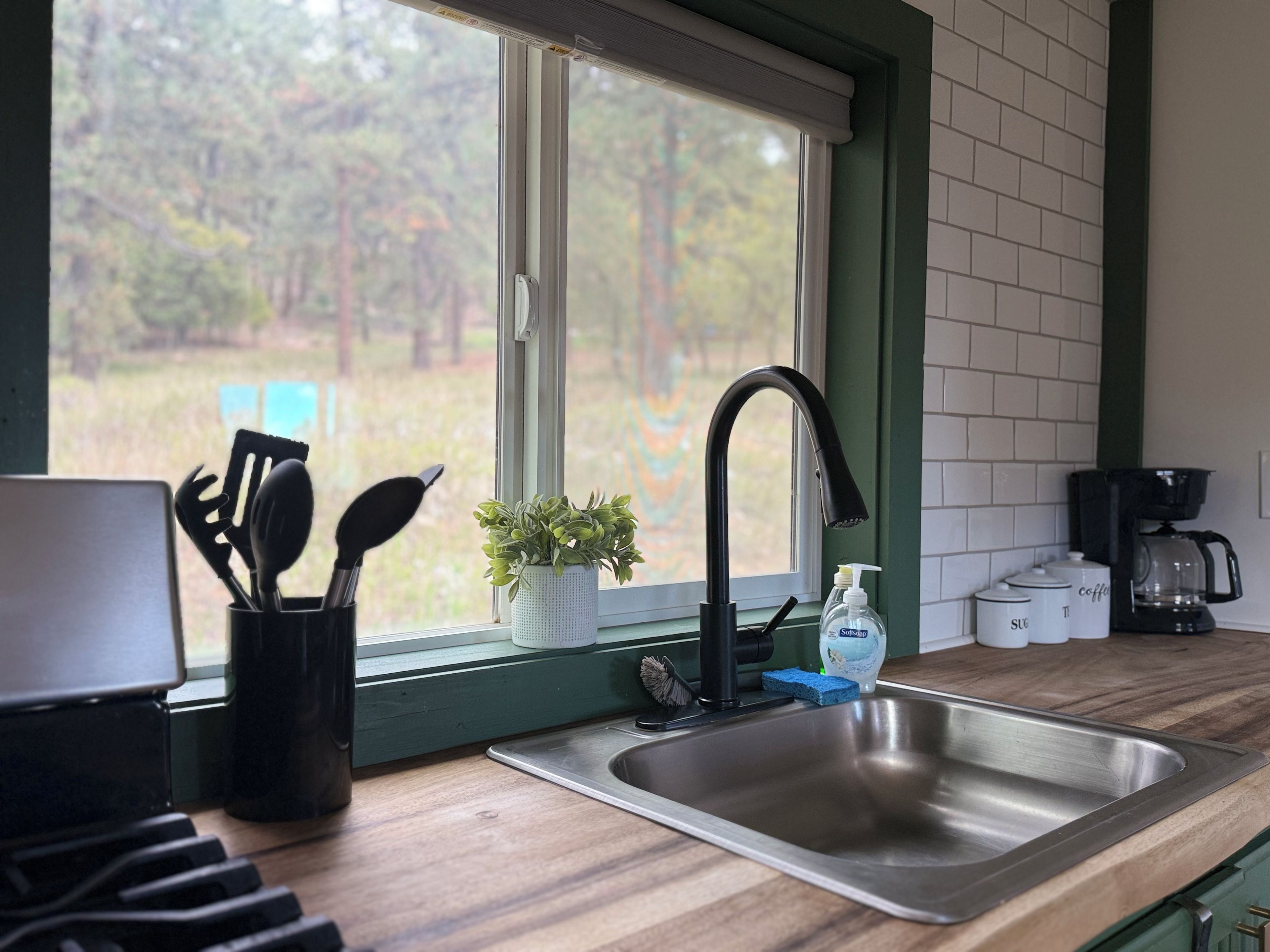 A kitchen with a stainless steel sink, a window with a view of trees, and a coffee maker on the counter.