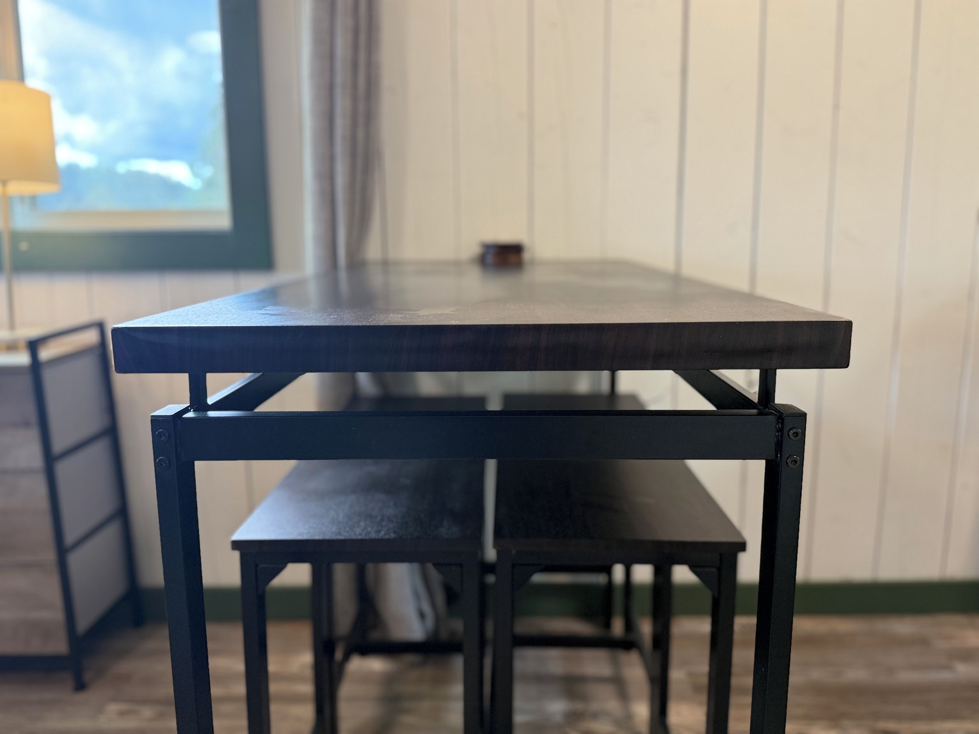 A table with a bench in front of a window with a view of the sky.