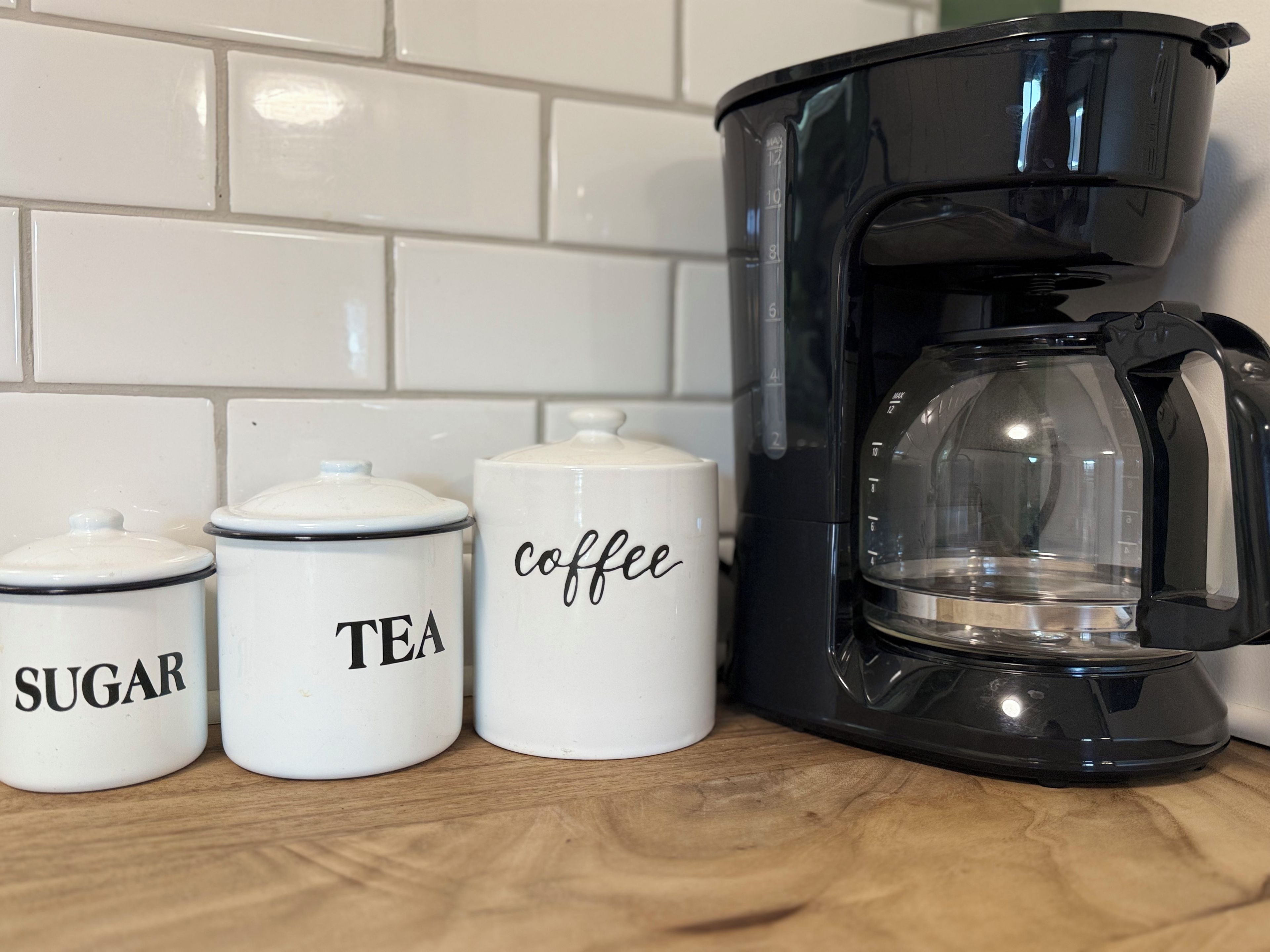 A kitchen counter with a coffee maker and three white containers labeled 'SUGAR,' 'TEA,' and 'coffee.'