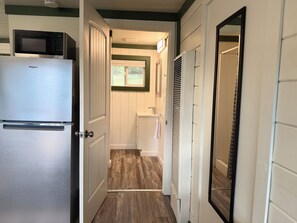 A narrow hallway with a white refrigerator, a microwave, and a white toilet.