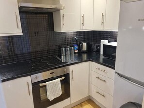 Eine Küche mit weißen Schränken, einer schwarzen Arbeitsplatte, einem Herd, einem Wasserkocher, einem Toaster und einem Kühlschrank.
