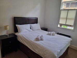 Habitació d'hotel amb llit, una tauleta de nit, una làmpada i una finestra.