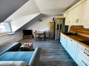 A compact living space with a sofa, a dining table, a kitchenette, and a television.