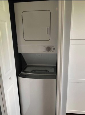 Una cambra de bugaderia petita amb rentadora i assecadora integrades, una finestra de dimensions reduïdes i una porta blanca.