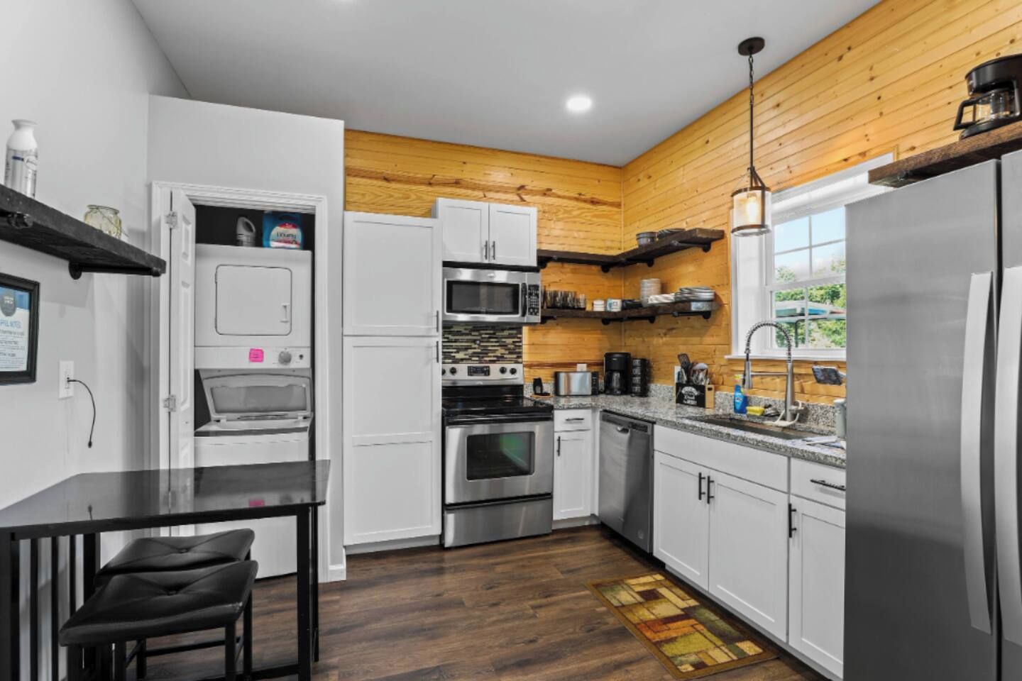 A modern kitchen with white cabinets, stainless steel appliances, and a wooden accent wall.