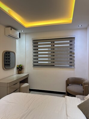 Un dormitorio moderno con cama, escritorio, silla, ventana con persianas y equipo de aire acondicionado.