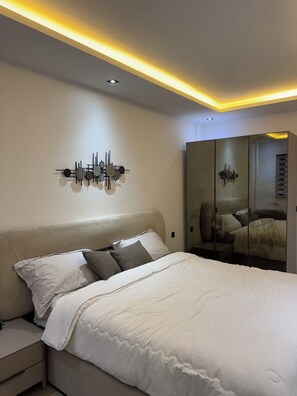 Un dormitorio moderno con cama, mesitas de noche, lámpara de pared y un armario con espejo.