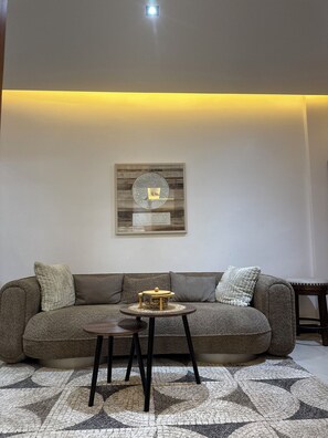 A living room with a sectional sofa, a small round table, and a wall-mounted picture frame. - Warn and Cozy 2-bedroom apartment in perfect Dakar-Almadies (Dakar)