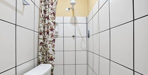 A bathroom with white tiled walls, a toilet, a shower with a handheld showerhead, and a floral curtain. - Apartamento em Cabo Frio Proximo da Praia do Pero (Cabo frio)
