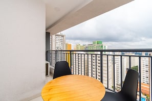 A balcony with a round table and two chairs, overlooking a cityscape with high-rise buildings. - Nex One Paraiso By Housi (São Paulo)