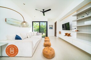 Ein modernes Wohnzimmer mit einer Couch, Hocker, einem Fernseher und einem Deckenventilator.