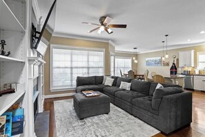 A spacious living room with a gray sectional sofa, a small ottoman, and a ceiling fan. - Lakefront w/ Private Dock / Pool Table +70" TV (Lexington)