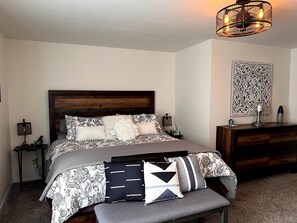 Una camera da letto con testiera in legno, un letto con biancheria a motivi, comodini con lampade, una cassettiera e un elemento decorativo a parete.